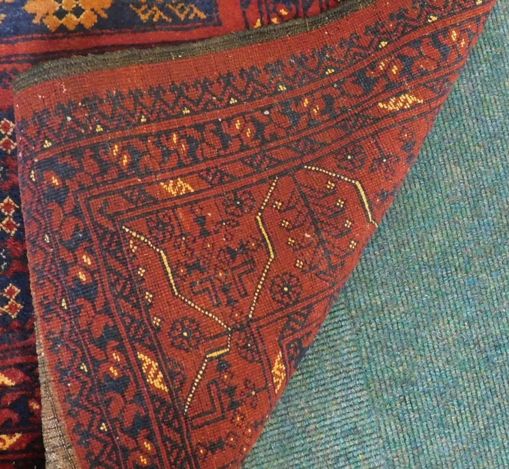 A Balouch type rug, with a design of medallions, in navy and cream on a red ground with multiple bo - Image 3 of 3