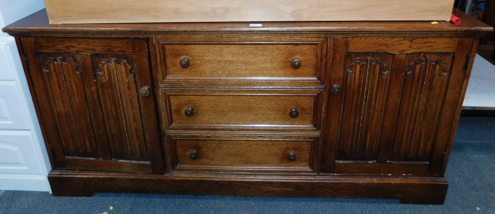 An oak veneered sideboard, of three drawers flanked by linenfold cupboard doors.