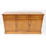 A Reprodux burr oak and cross banded sideboard, of three drawers over cupboard doors, raised on a pl