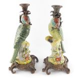 A pair of Meissen style porcelain and metal figural candlesticks modelled as parrots, perched on tre