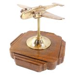 A brass desk stand modelled as a World War II bomber plane, raised on a shaped oak base, 19cm wide.