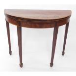 A George III mahogany and rosewood cross banded demi lune fold over card table, raised on tapering