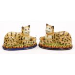 A pair of Staffordshire style seated cats, each cat with ball on a green stepped base on blue circul