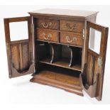 A 1920s oak smoker's cabinet, with two partially glazed doors opening to reveal four fitted drawers