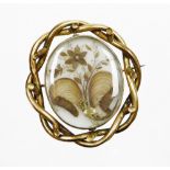 A Victorian memorial brooch, with central oval panel with locks of hair and flower type design, in a