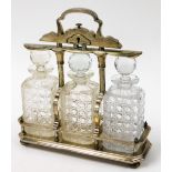 A late 19thC silver plated tantalus, with three cut glass decanters, in a raised key lock silver pla