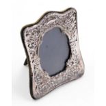 A silver photograph frame, with floral scroll embossed decoration and blank cartouche, oval aperture