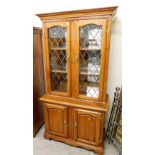 A stained pine display cabinet, with two astragal glazed doors and two bookshelf top above two cupbo