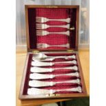 A cased set of silver plated fish knives and forks, in an oak case with brass central shield crest.
