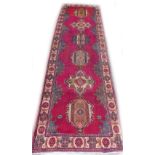 A Persian runner, with a design of medallions on a red ground, one wide border, 325cm x 98cm.