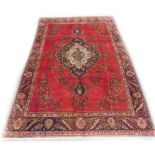 A Persian rug, with a central pole medallion in navy, on a red ground decorated with flowers,