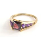 A 9ct gold dress ring, with square set red faceted stone and amethyst set tension shoulders, the