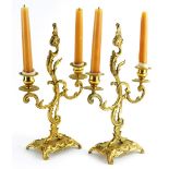 A pair of 19thC continental brass two branch candlesticks, ornately decorated with scrolls,