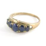 A dress ring, set with five oval cut dark blue faceted stones, pierced and oval setting on a