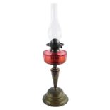 A 19thC oil lamp, with a cranberry coloured central reservoir, above a brassed pedestal base,