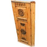 A heavily carved rustic pine hanging cupboard, with roundels of carved floral rosettes and a part fi