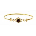 A 9ct gold hinged bangle, with central oval cut garnet in floral cluster setting with scroll design