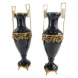 A pair of 19thC continental black glass two handled urns, with shaped brass handles, and a moulded b