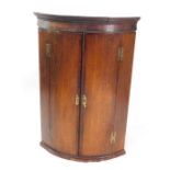 A George III oak and mahogany cross banded wall hanging corner cupboard, the out swept pediment over