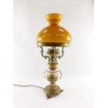 A 20thC oil lamp style electric table lamp, with orange glass shade on a brass three prong support,