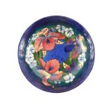 A Moorcroft pottery bowl decorated in the Frilled and Slipper Orchid pattern, against a blue ground,