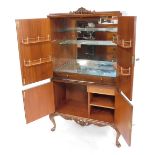 A mid century burr walnut cocktail cabinet, the foliate carved top over a pair of doors, opening to