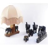 A group of ebony carved elephant ornaments, and a table lamp with two elephants to the base, frilled