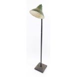 An industrial mid century standard lamp, with green metal shade, on a black metal pole and square ba