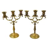 A pair of brass candelabra, each with three shaped arms, on a turned column and dome foot.