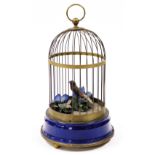A 20thC brass and tin plate musical automaton bird cage, containing a feather clad bird and various