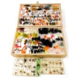 A collection of fishing flies contained in a wooden reservoir fly box, including salmon flies and tu