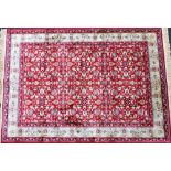 A Kashmir red ground rug, decorated with a floral design, within repeating floral borders, 87cm x 13