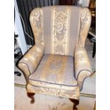 A wingback armchair, upholstered in blue and gold fabric, on cabriole legs terminating in pad feet,