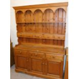 A pine dresser, the top with moulded cornice, above an arrangement of shelves, drawers, etc., the ba