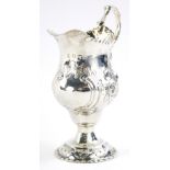 A George III silver cream jug, the helmet shaped body with ear handle repousse decorated with scroll
