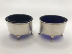 Pair of Oval Silver hallmarked salts each on three scroll feet with Blue glass liners