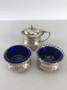 Two silver salts and matching mustard pot with repousse decoration and blue glass liners, hallmarked