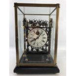 A skeleton movement rolling ball table clock with cloisonné posts and finials in glass case. Clock