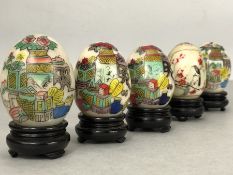 Collection of five painted marble Chinese eggs on wooden stands