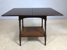 Small mahogany fold out games table on turned legs with shelf under