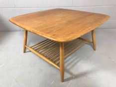 Ercol light finish coffee table of rounded square form on turned legs with magazine rack under,