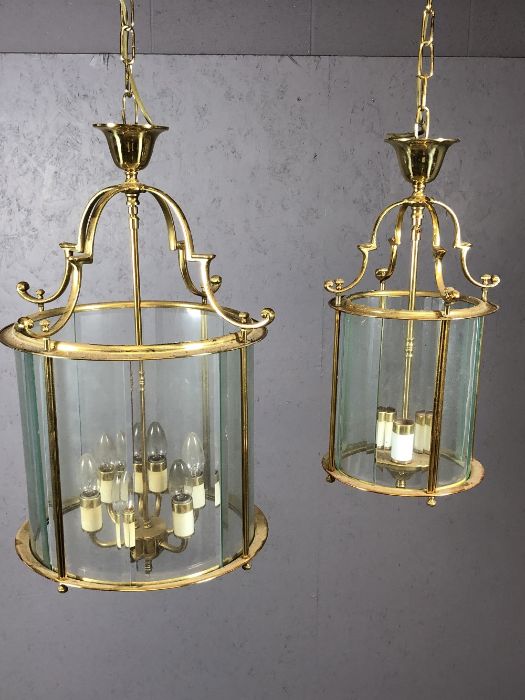 Two brass pendant lights with round glass shades, the larger approx 65cm in drop