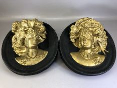 Pair of gilt and black circular plaster decorative wall plaques, each depicting a female head in