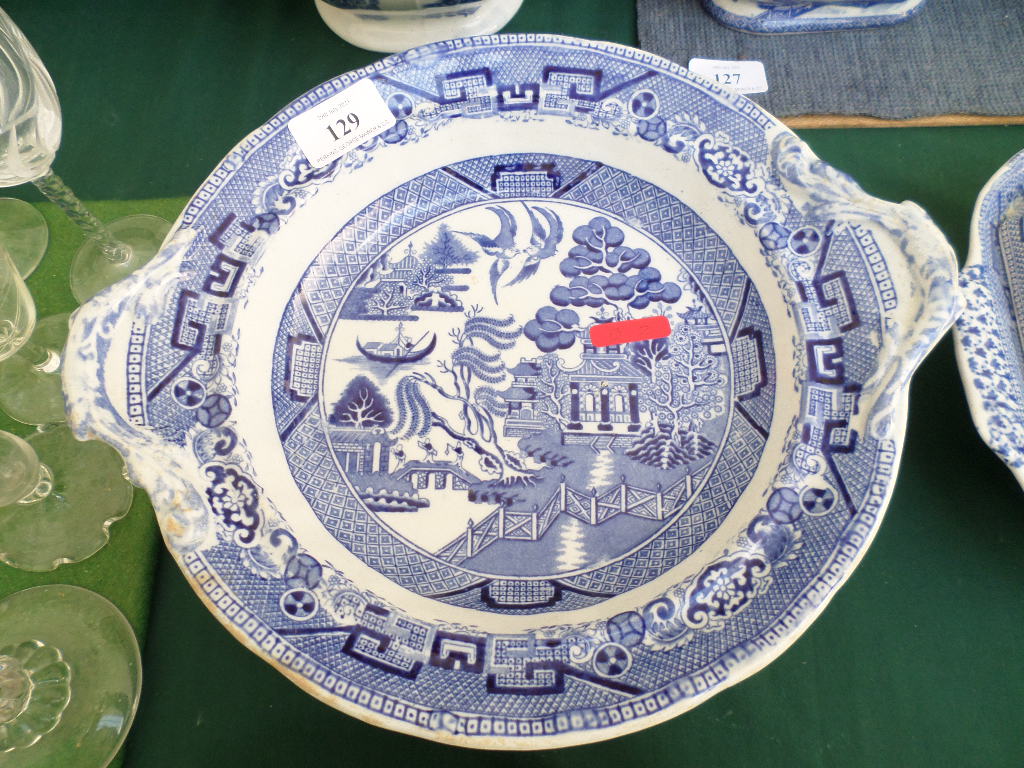 Circular blue and white willow patterned serving dish on circular raised plinth and plate