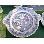 Circular blue and white willow patterned serving dish on circular raised plinth and plate