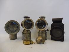Three nickel plated carbide lamps, a brass bicycle bell, a brass cased voltmeter and a rear lamp.