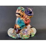 A colourful ceramic figure group of a lady and gentleman riding a tandem bicycle.