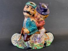 A colourful ceramic figure group of a lady and gentleman riding a tandem bicycle.