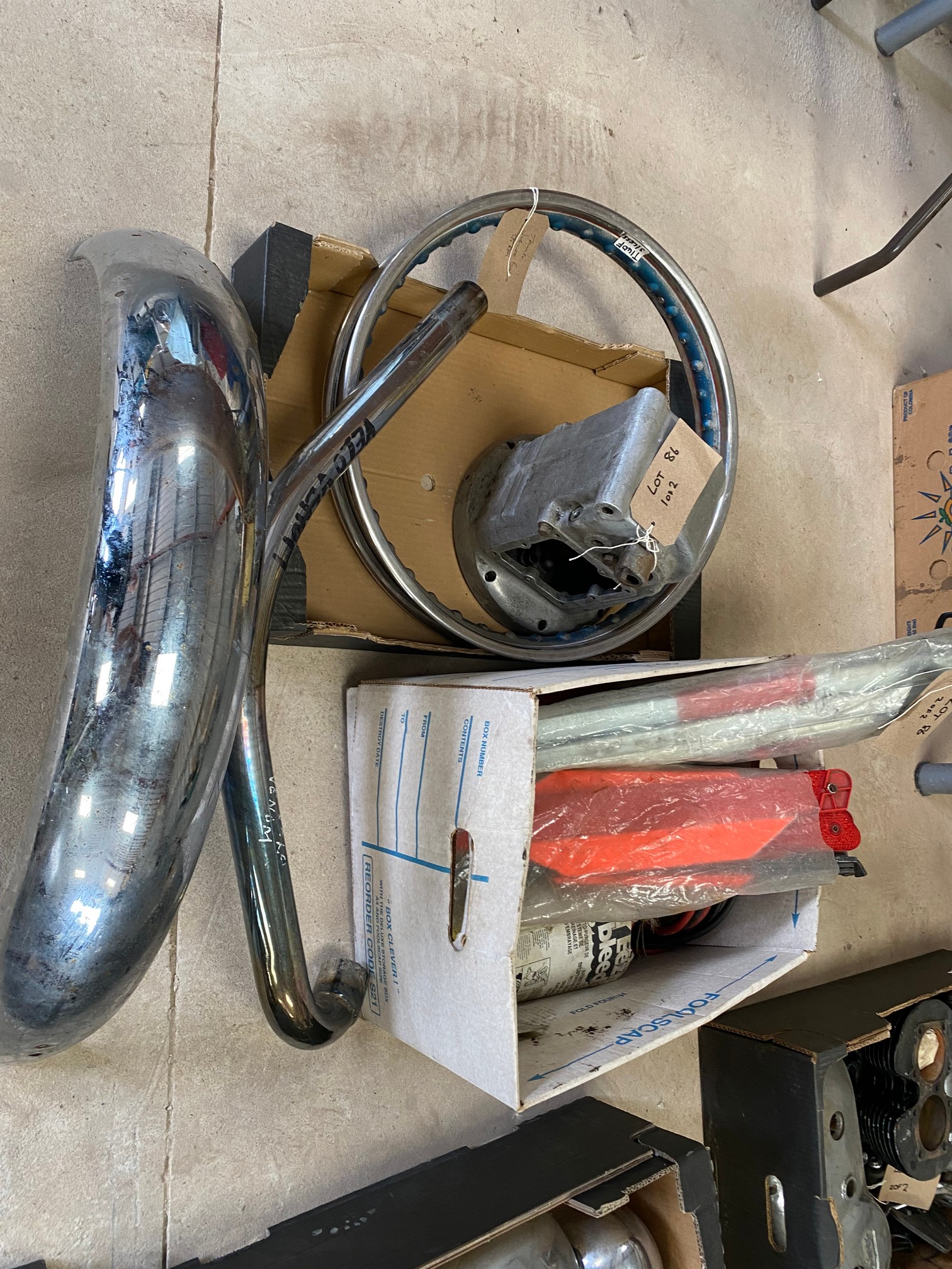 Two boxes of spares including a Velocette Venom exhaust down pipe, Triumph Bonneville Jubilee S/S