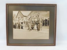 A framed and glazed early photograph of a garage/petrol station, displaying petrol pumps, globes,